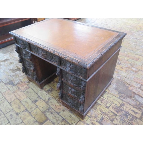 77 - An oak kneehole writing desk with tooled leather top and ornate 'Green Man' carved drawers, 107cm wi... 