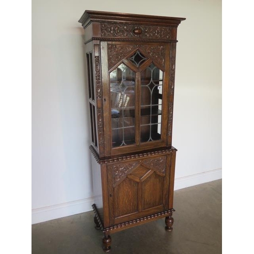 89 - A carved oak 1930s cabinet with a leaded glazed door above a cupboard door on turned feet with a Rob... 