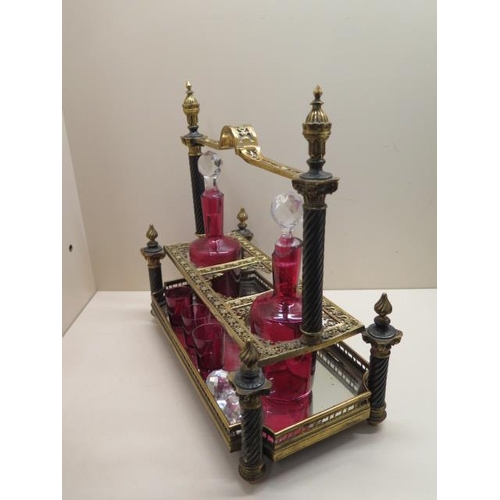 488 - An ornate gilt metal 3 bottle cranberry glass liquor stand with 2 bottles, a stopper and 3 glasses. ... 