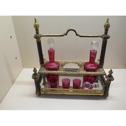 488 - An ornate gilt metal 3 bottle cranberry glass liquor stand with 2 bottles, a stopper and 3 glasses. ... 