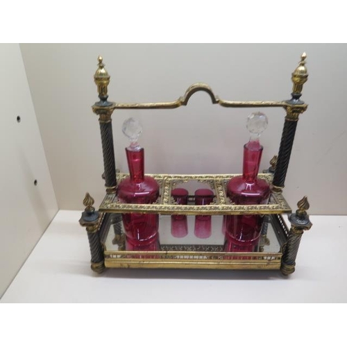 488 - An ornate gilt metal 3 bottle cranberry glass liquor stand with 2 bottles, a stopper and 3 glasses. ... 