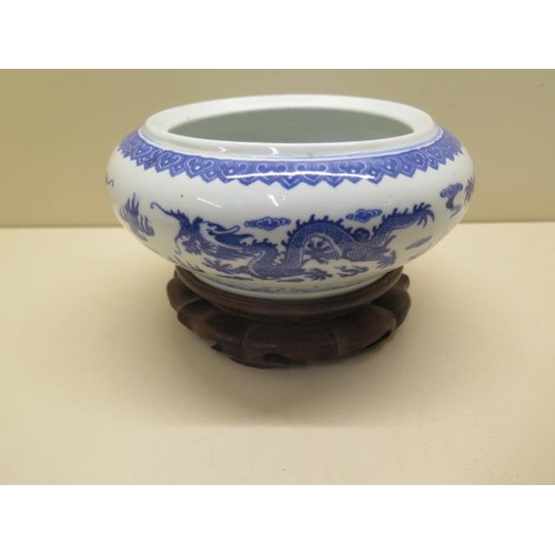 444 - An oriental blue and white dragon bowl on a hardwood stand, total 14cm tall x 22cm diameter, no obvi... 