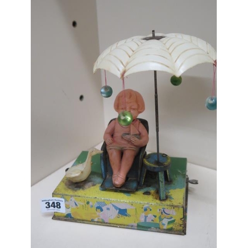 348 - A tinplate model of a girl in chair rocking, with rotating umbrella and squeaking goose beside her