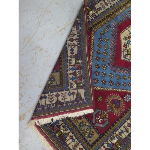 394 - A hand knotted woollen rug with a red field - 220cm x 115cm - generally good