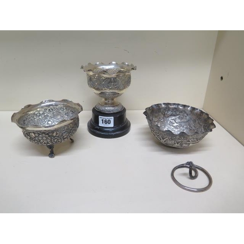 160 - Three Eastern white metal embossed bowls, one on a wooden stand, one with broken base the other on a... 