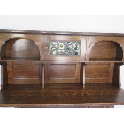 566 - A Liberty Arts & Crafts oak dresser with a glazed single door and two shelves over the base with a s... 