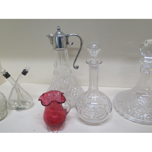 404 - A moulded glass claret jug with a plated top, four glass decanters, oil bottle and a cranberry glass... 