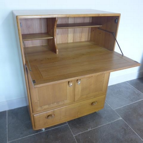 153 - An Ercol Golden Dawn blonde elm cabinet with a drop down front above two cupboard doors and a base d... 