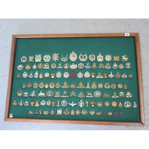 402 - A mounted and framed display of British Military cap badges - 117 in total - 65cm x 95cm