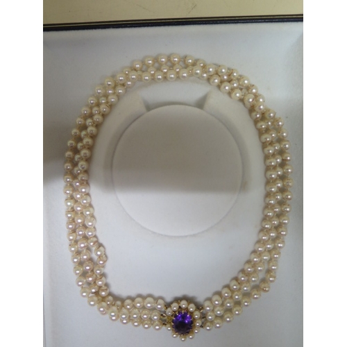 65 - A triple string pearl necklace with a 9ct yellow gold clasp set with central amethyst surrounded wit... 