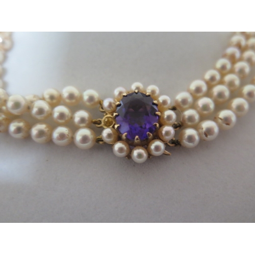 65 - A triple string pearl necklace with a 9ct yellow gold clasp set with central amethyst surrounded wit... 