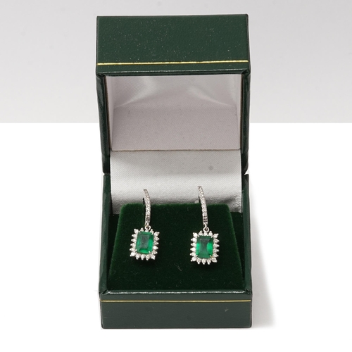 83 - A pair of 18ct white gold drop earrings set with emerald-cut emeralds, surrounded by round brilliant... 