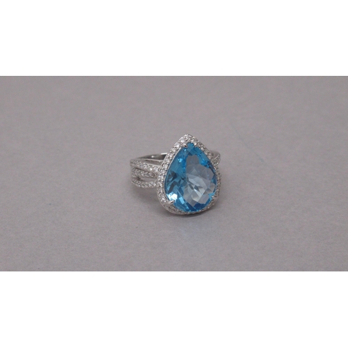 100 - An exciting 18ct white gold ring set with a pear-shaped blue topaz and halo of round brilliant cut d... 