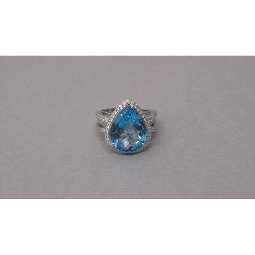 100 - An exciting 18ct white gold ring set with a pear-shaped blue topaz and halo of round brilliant cut d... 