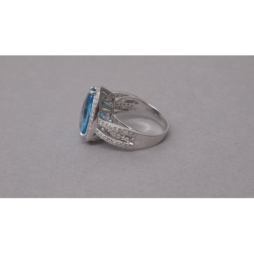 100 - An exciting 18ct white gold ring set with a pear-shaped blue topaz and halo of round brilliant cut d... 