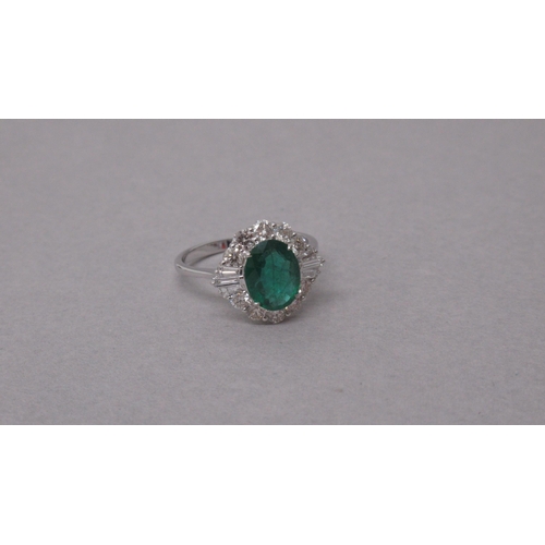 102 - An 18ct white gold ring set with an oval-cut emerald surrounded by a halo of diamonds - Emerald 1.38... 