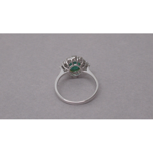 102 - An 18ct white gold ring set with an oval-cut emerald surrounded by a halo of diamonds - Emerald 1.38... 