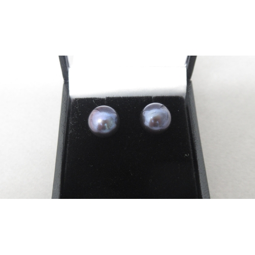 92 - A pair of 9ct yellow gold studs set with oblate spheroid black cultured pearls, with reflections in ... 