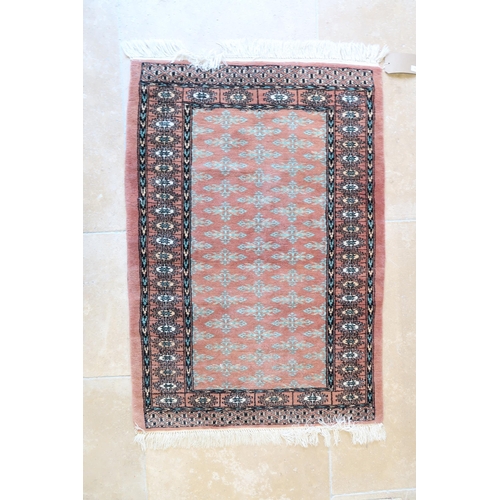 591 - A small hand knotted woollen rug with a pink field - 130cm x 80cm - good condition