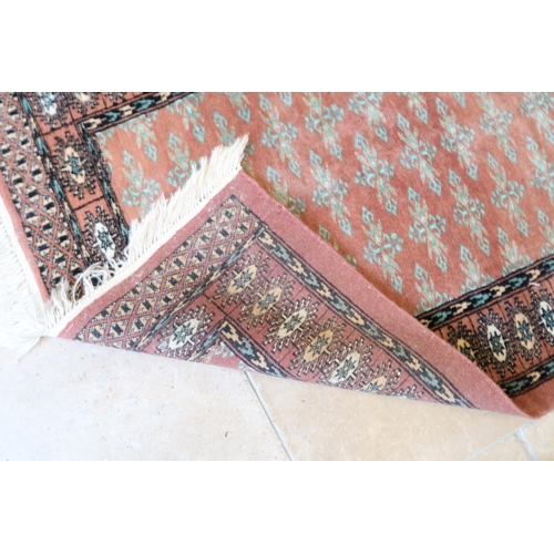 591 - A small hand knotted woollen rug with a pink field - 130cm x 80cm - good condition