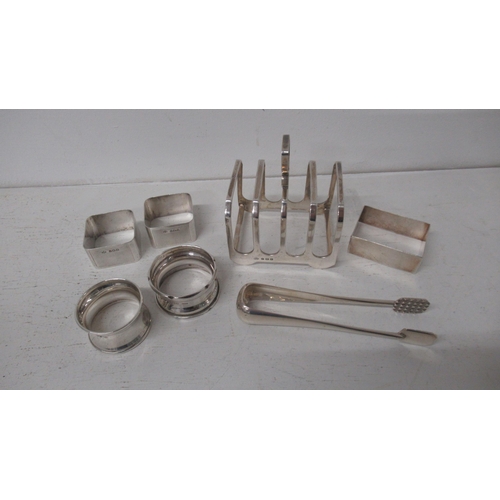 306 - Seven silver items including toast rack, sugar tongs and five napkin rings - approx weight 7.8 troy ... 