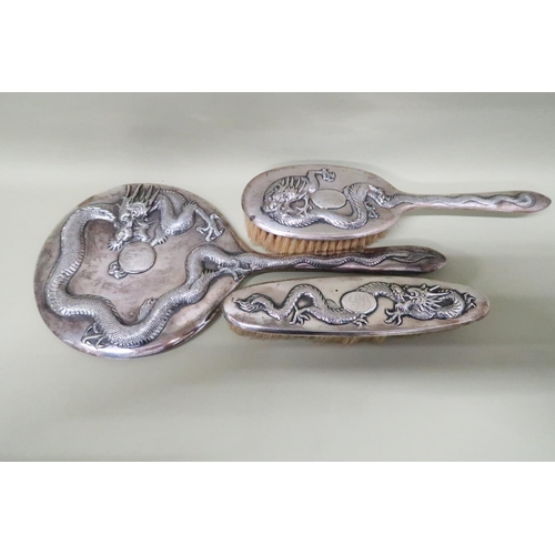 405 - A hand mirror, hairbrush, clothes brush - all in Chinese silver decorated with dragons