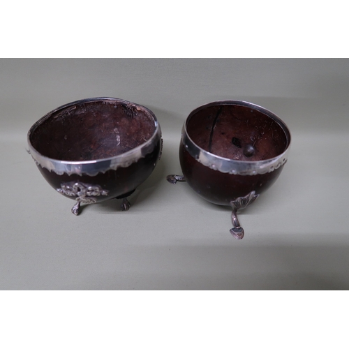 365 - Two coconut cups with engraved decoration to white metal mounts, both raised on three short feet