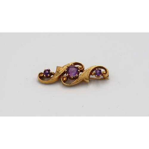 62 - A 9ct yellow gold bar brooch with three amethysts set in scrolling background, approx 5.26 grams