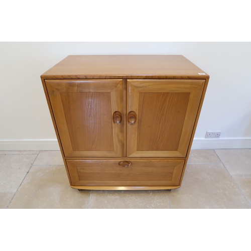 649 - An Ercol blonde elm mid 20th Century cabinet of two doors, single fall from below with sliding tray ... 