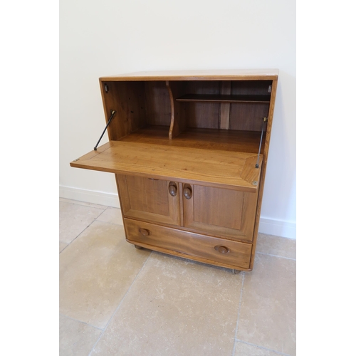 650 - An Ercol blonde elm mid 20th Century cabinet with fall front to top over two cupboard doors with a s... 