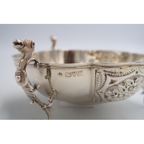 338 - A hallmarked silver sweet meat dish raised on three supports with animal head handles, embossed foli... 