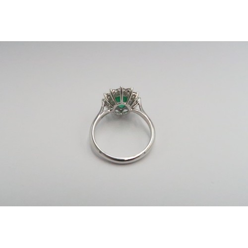  A platinum emerald and diamond dress ring - The central oval cut emerald surrounded by 12 diamonds -... 