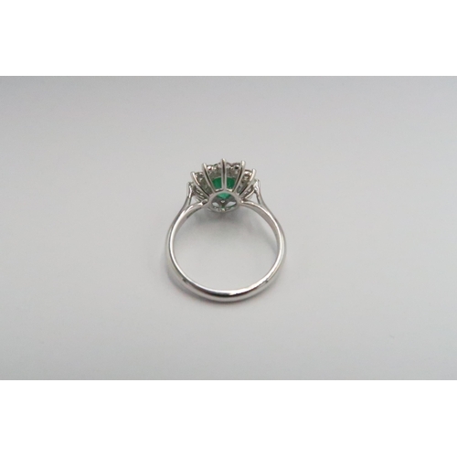 204 - A platinum emerald and diamond dress ring - The central oval cut emerald surrounded by 12 diamonds -... 