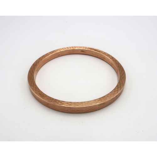 218 - A 9ct rose gold bangle of circular form with engine turned decoration, 73mm diameter, 15.2g.