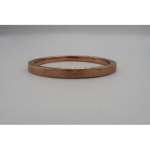 218 - A 9ct rose gold bangle of circular form with engine turned decoration, 73mm diameter, 15.2g.