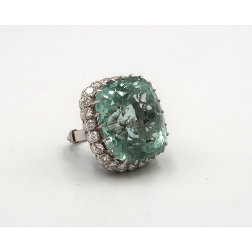 An aquamarine and diamond cluster ring. The cushion cut aquamarine estimated 74cts. Within a scalloped surround of 24 brilliant cut diamonds. Estimated total weight 3.36cts. Estimated G/H VS2/SI1. Tests gold 18ct. Ring size K. With sizing beads the the band. Weight 31.89 grams. Excellent condition.