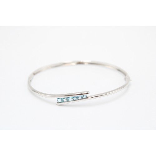 A 9ct White Gold Bangle, With a Central Princess Cut Blue Stone Bypass Section of Five Graduating St... 