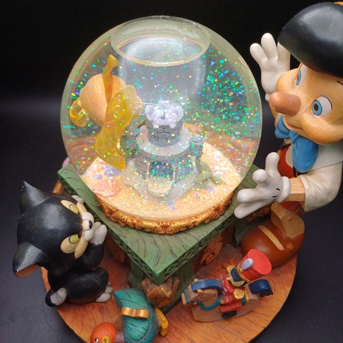 102 - Disney Snow Globe with Pinocchio looking into the globe where the fish in side rotas when you wind t... 