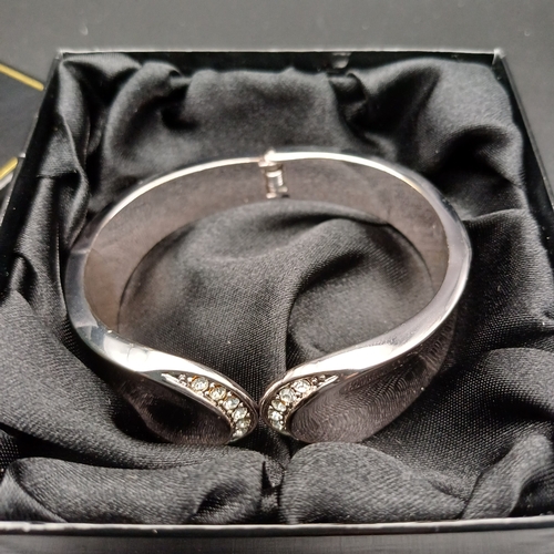 83 - In original box we have a stunning heavy silver coloured metal sprung hing bangle with white stone s... 