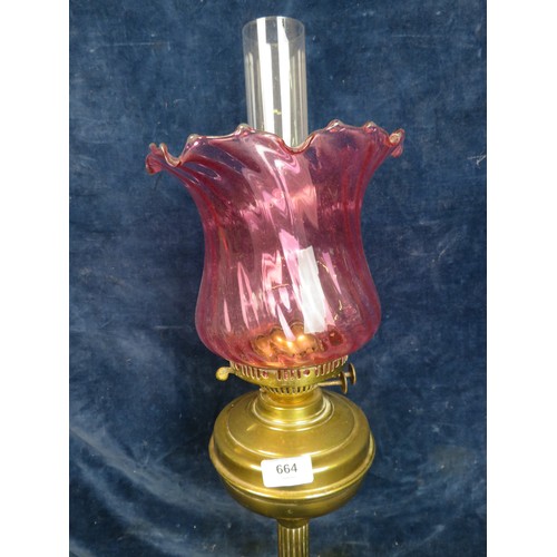 664 - A brass pedestal oil lamp with chimney and cranberry glass shade.