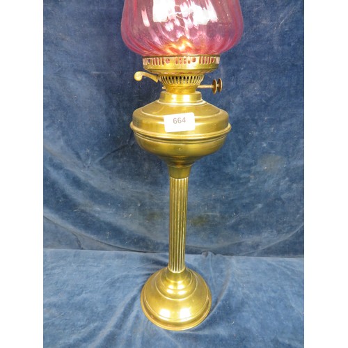 664 - A brass pedestal oil lamp with chimney and cranberry glass shade.