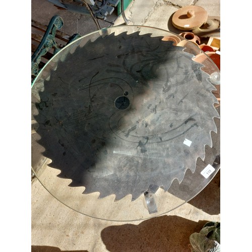 119 - CIRCULAR TABLE WITH SAW BLADE AND GLASS TOP, DIAMETER 71CM APPROXIMATLEY.