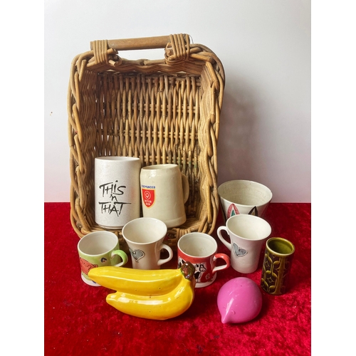 38 - A wooden basket containing a collection of mugs and some ceramic bananas