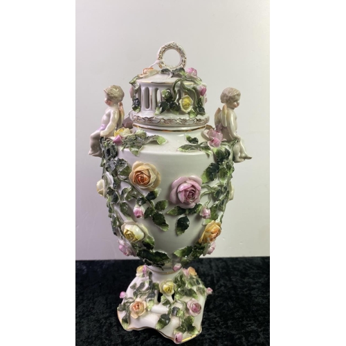 525 - Tall 19th century porcelain lidded urn with cherubs. Heavily decorated with roses. Slight damage to ... 