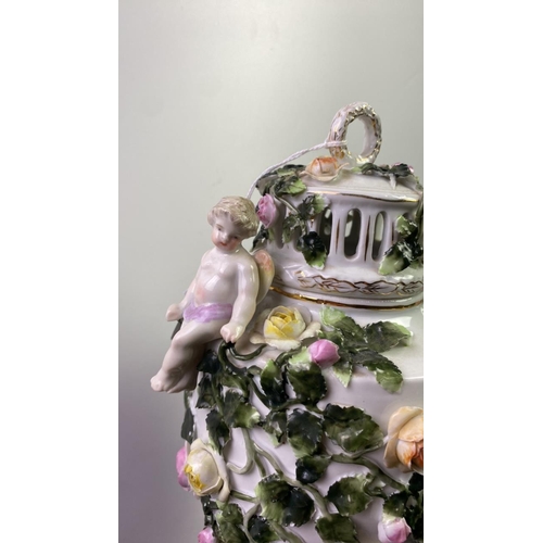 525 - Tall 19th century porcelain lidded urn with cherubs. Heavily decorated with roses. Slight damage to ... 