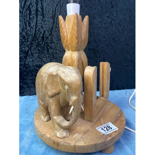 128 - A quirky carved wooden circular lamp base on matching wood feet, featuring an elephant by a tree, wi... 