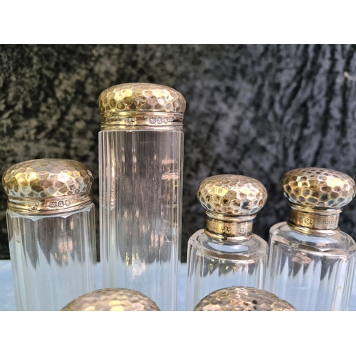 745 - Six matching silver topped glass dressing table bottles of varying size with hammered design lids, a... 