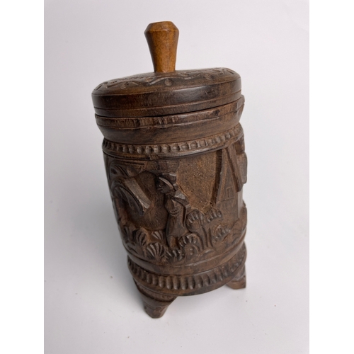 400 - Hand carved wooden lidded cylindrical container with carved village scene, likely African, 16.5cm ta... 