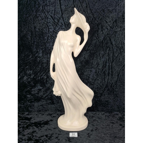 31 - Tall, white glazed ceramic figurine of a woman wearing a flowing dress and holding her hat. Approx H... 