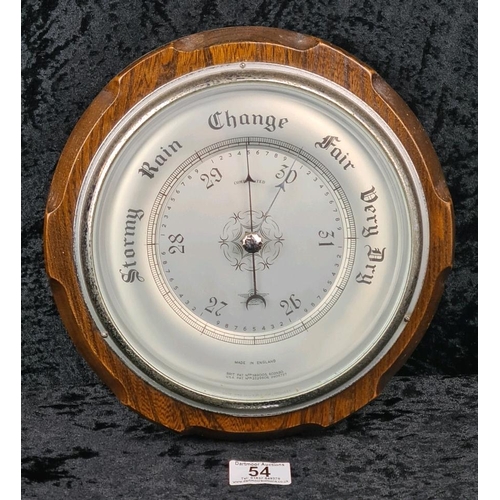 54 - Aneroid barometer with a silvered dial, a brass bezel, and housed in a carved wooden case. Approx Di... 